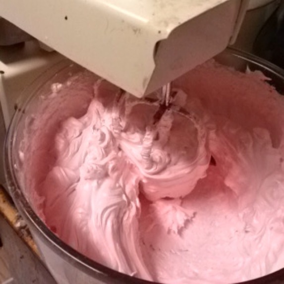A close up of a pink meringue in a bowl under a mixer